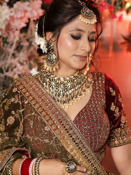 A close-up of a bride in a deep green and maroon velvet lehenga, focusing on the heavy polki and kundan necklace.