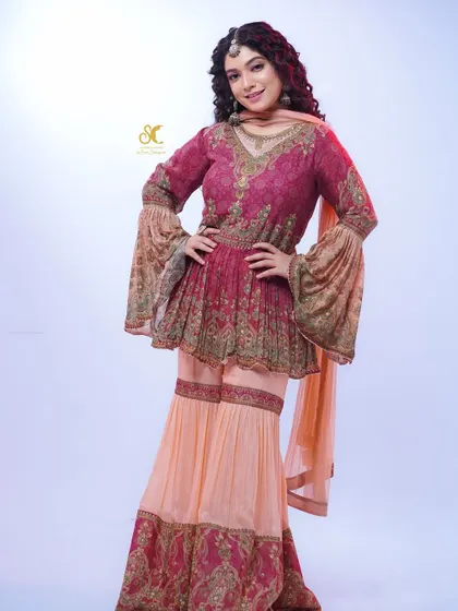 A full-length view of Priyanka Thimmesh wearing the magenta and peach sharara set. The combination of the flared sleeves and wide-legged pants creates a dramatic and festive silhouette.