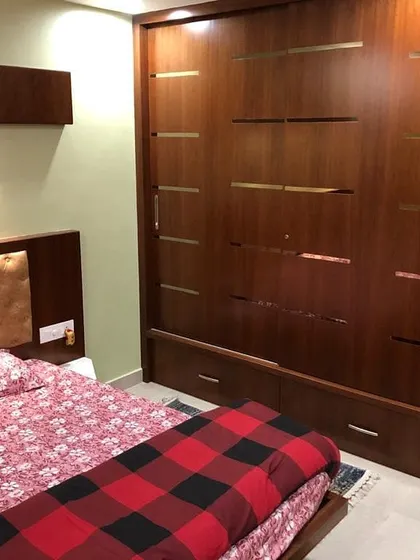 An interior view of a bedroom, showcasing custom wardrobe design. The dark wood finish with metallic inlay details reflects a modern and sophisticated approach to interior furnishings and storage solutions.