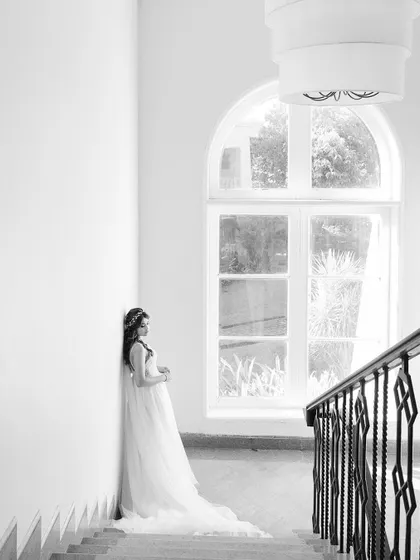 A serene bridal portrait on a grand staircase in Goa. The high-key black and white processing emphasizes the bride's elegant white gown and the architectural beauty.