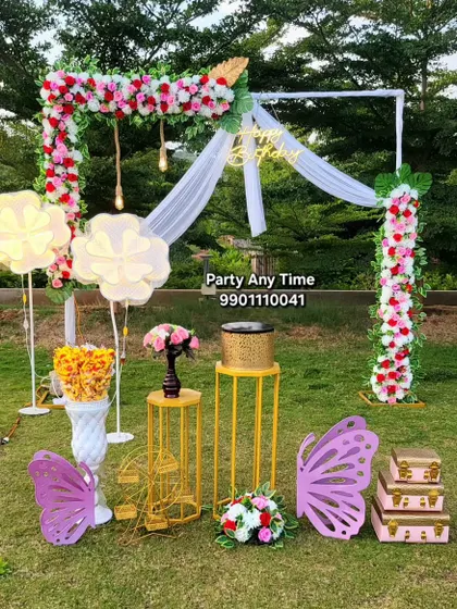 I can set up decorations for outdoor events too. This beautiful garden setup for a special occasion includes a floral arch with draping, large butterfly and flower props, and elegant plinths for cakes or displays.