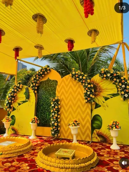 A fun and creative sunflower-themed Haldi stage. The backdrop features large sunflower prints and a floral arch, creating a bright and happy space for photos.