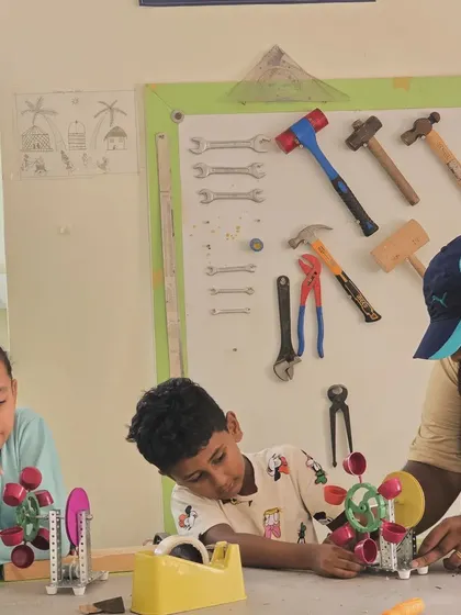 An instructor helps students assemble a mechanical water turbine, explaining how gears and moving parts work together to generate motion.