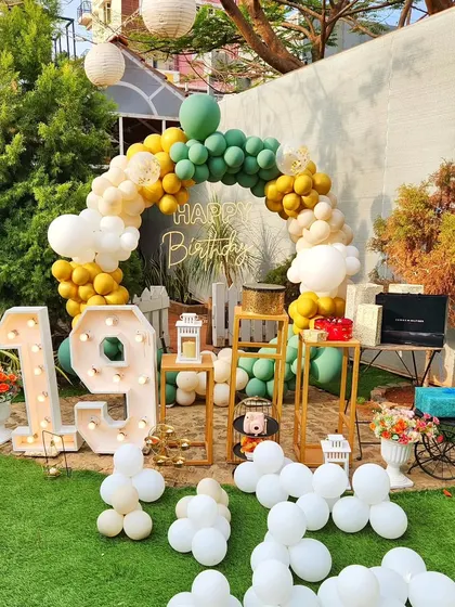 An outdoor 19th birthday celebration with a green and gold balloon arch and large marquee numbers.