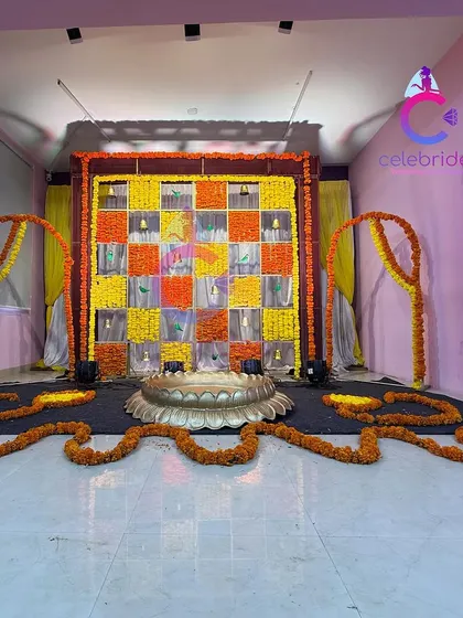 A creative Haldi backdrop with a checkerboard pattern of multi-colored marigolds. The hanging bells and side arches add a festive touch.