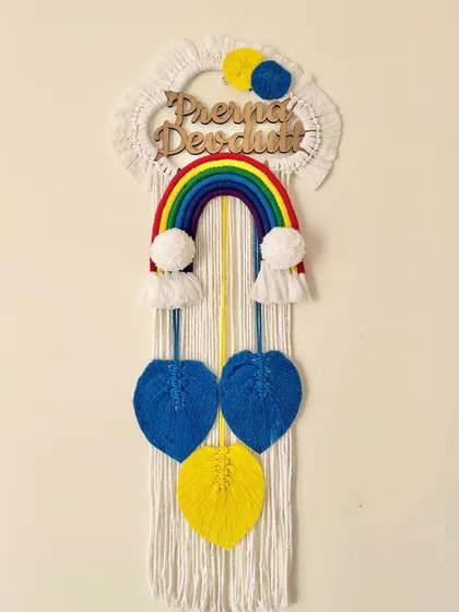 A custom rainbow name hanging for Prerna and Devdutt, featuring a classic rainbow, pom-poms, and colorful hanging leaves.