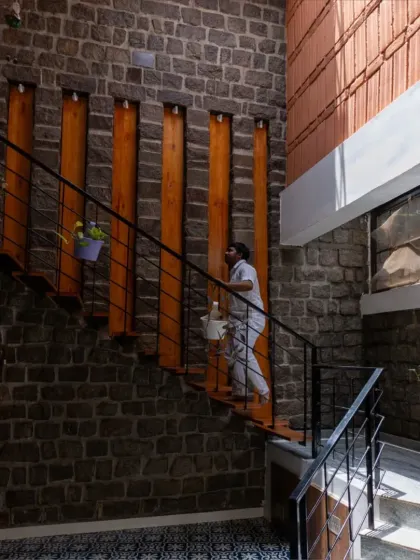 The floating staircase against a rugged stone wall is a central feature in the Gifty Residence. The contrast between the dark stone and the warm wood of the steps creates a dramatic and beautiful focal point.