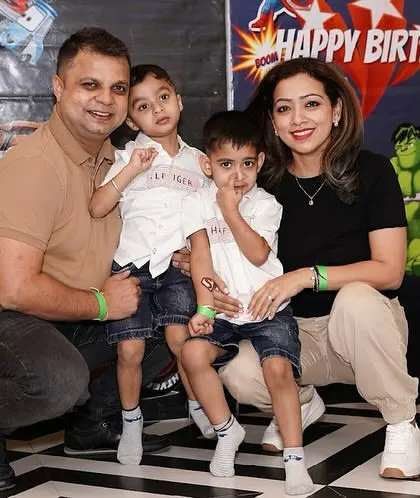 A happy family poses at a superhero and Cars themed birthday party, surrounded by colorful balloons.