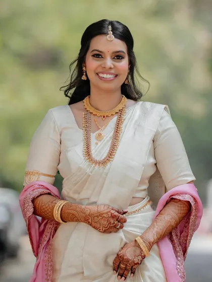 A full-length view of the bride in her simple yet stunning white and gold saree. The makeup is intentionally understated to complement the minimalist aesthetic.