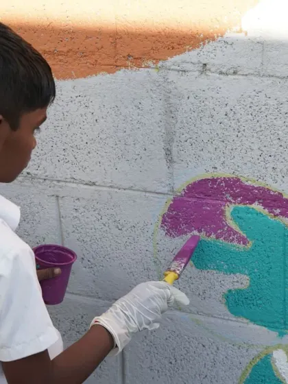 A young artist carefully applies a vibrant teal paint inside the lines of a butterfly wing. This close up highlights the focus and dedication that even the youngest participants bring to our community art projects.
