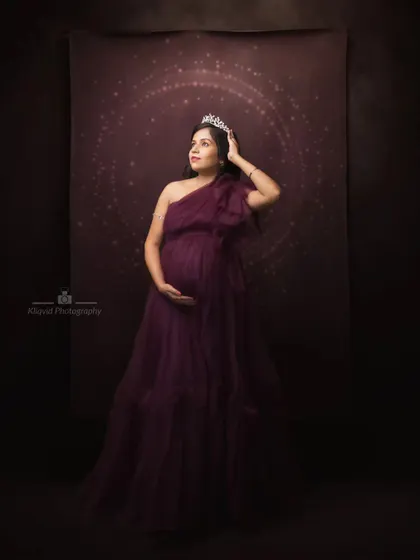 A regal portrait in deep purple. Crowned and poised, this mother-to-be looks out from a celestial backdrop, a true queen in her own right.
