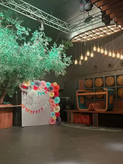 A simple and elegant photo booth for a Lohri celebration. The backdrop is decorated with colorful paper fans and a "Samvid di Lohri" message.
