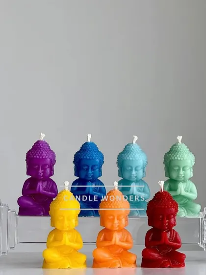 The chakra Buddha candles displayed on a clear stand, showing off their vibrant rainbow colors.