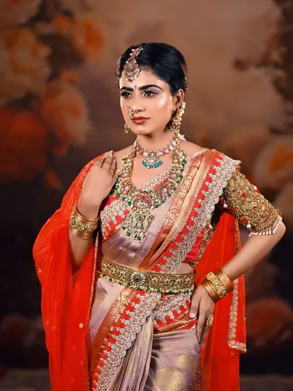 A regal pose showcasing the bride's complete attire. The floral backdrop complements the colors of her saree and the intricate embroidery on her blouse.