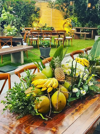 A long wooden table adorned with a runner of fresh coconuts, bananas, pineapples, and local foliage. This zero-waste setup proves that sustainable decor can be incredibly lush and opulent.