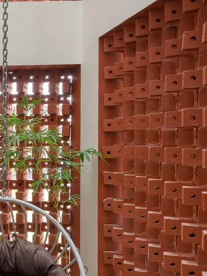 The brick jali wall encloses a cozy balcony space, complete with a hanging swing chair. It's a perfect spot for relaxing, surrounded by plants and filtered sunlight.
