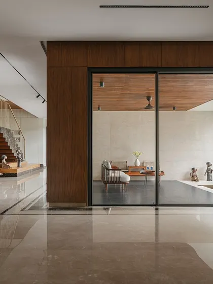 This view from the main living area of Villa Shakthi looks towards the formal drawing room. The polished marble floors and wood-paneled walls create a sophisticated material palette, while the open plan maintains a visual connection across different zones of the house.