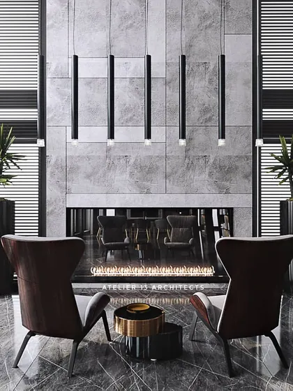 A cozy seating area in front of a grand fireplace set in a grey marble wall. The high-back armchairs create an intimate conversation spot within a larger, double-height space, showcasing our skill in creating different scales of experience.