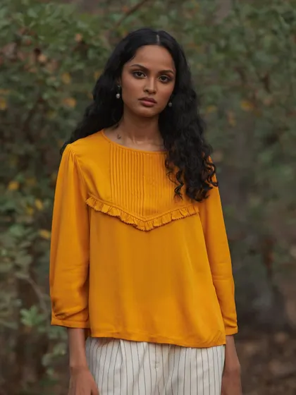 An outdoor fashion shoot for a clothing brand. The vibrant yellow top stands out against the natural green background, creating a fresh and lively image.