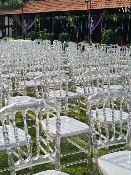 Rows of elegant transparent ghost chairs set up on a lawn for an outdoor ceremony. This choice of seating adds a touch of modern sophistication and doesn't obstruct the view of the beautiful decor.