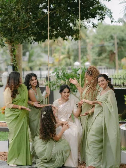 The bride, seated on a swing, is surrounded by her smiling bridesmaids. This candid and interactive group photo is full of life and captures the strong bond of their friendship.