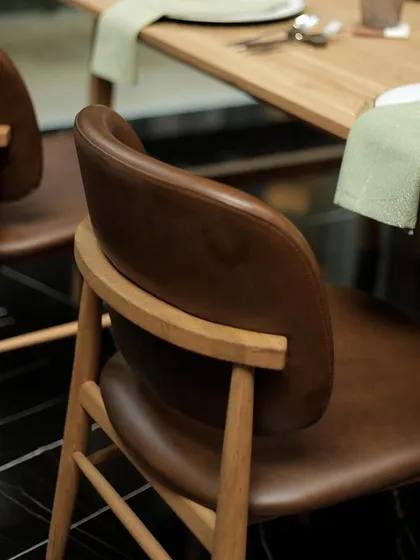 The gentle curve of a leather-upholstered dining chair back. Crafted with care and attention to detail, our dining sets are designed to make every gathering feel special and comfortable.