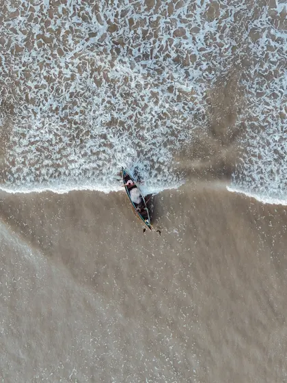 A top-down drone shot of a lone boat meeting the waves on the shore. The patterns in the sand and foam are mesmerizing from this angle.