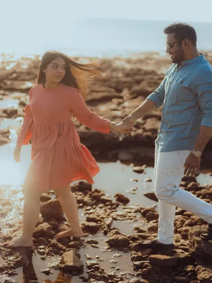 A romantic walk through shallow waters and rocks on the beach, holding hands as the wind catches her dress.