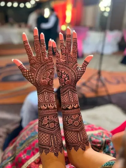 A full bridal design with a rich, dark stain, photographed at an evening event. The intricate patterns are visible even in low light.