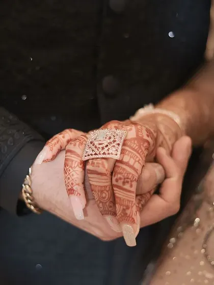 A close-up on the hands, showing the engagement ring and the intricate mehendi. This detail shot tells a story of commitment and tradition.