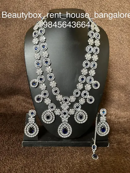 A modern CZ stone set featuring striking blue sapphire-like stones. The rental includes a long necklace, earrings, and a maang tikka.