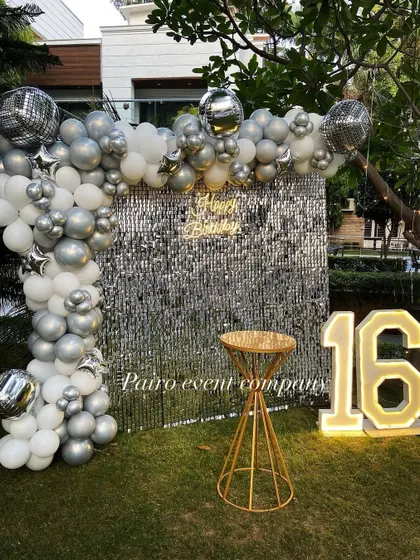 I create chic and modern setups perfect for a 16th birthday or any stylish celebration. This outdoor party features a stunning silver sequin wall for the perfect photo backdrop, a balloon arch with disco ball accents, and large glowing numbers to mark the special age.