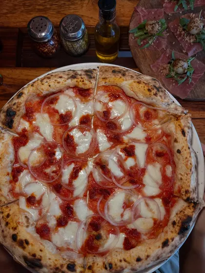 The Goan Sausage pizza sits next to a board of prosciutto, a feast for meat lovers.