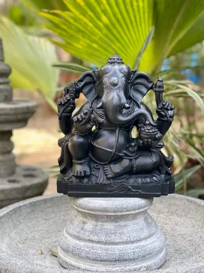 This Ganesha statue, carved from Krishna shila stone, is shown on a stone plinth, ready to become a centerpiece in a home or garden.