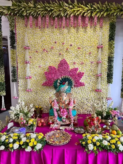 A beautiful floral wall of white flowers serves as the canvas for this Ganpati setup. A pink lotus design and hanging flower strings add a touch of color and traditional elegance.