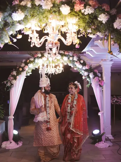 The newlyweds walk hand-in-hand under a beautifully decorated floral archway with a chandelier.