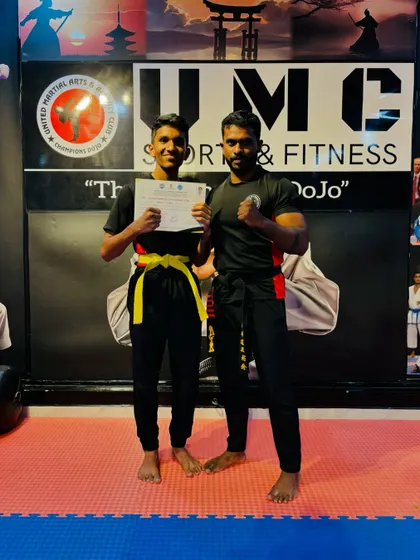 A student and coach pose after a successful belt grading. We celebrate every step of our students' progress.