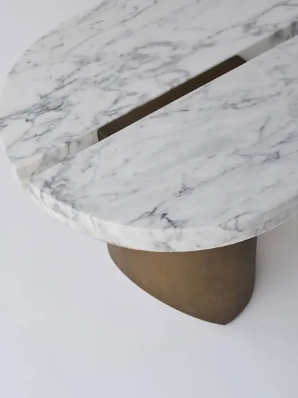 A close-up of the SPLIT center table, which features a solid Statuario marble top elegantly divided by a metal accent. The base is crafted from cast metal, providing a sculptural foundation.