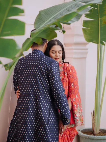 A quiet, intimate moment of a couple embracing, framed by the leaves of a large plant.