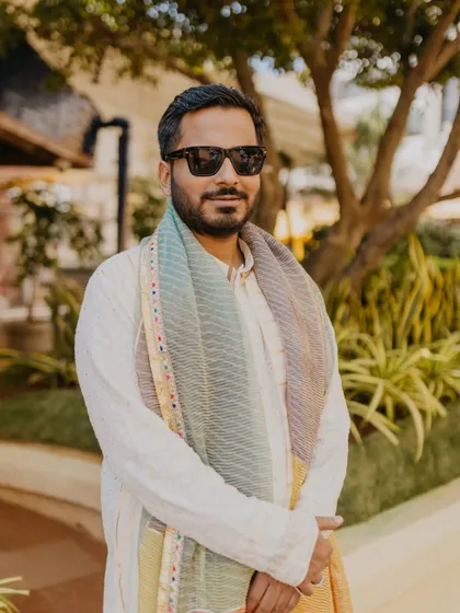 A stylish portrait of the groom in his traditional white kurta and colorful scarf. His cool sunglasses and relaxed pose give him a modern yet classic look.