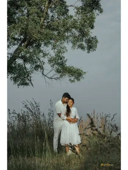 A couple embraces under a tree in a field, a classic and timeless romantic portrait.