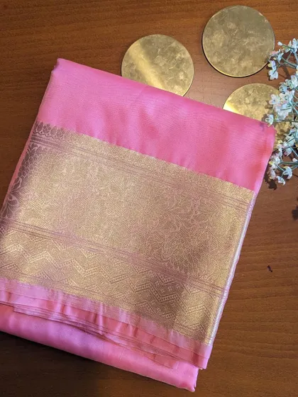 The pink Kora Organza saree is soft and romantic. The wide gold border adds a touch of grandeur to the delicate fabric.