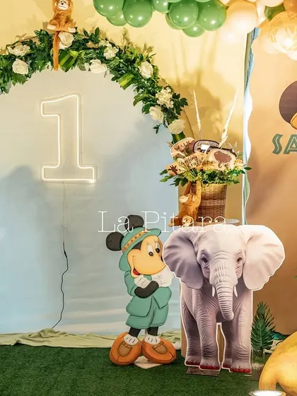 A photo corner with a floral and balloon arch, a neon '1', and cutouts of Mickey, Minnie, and an elephant.