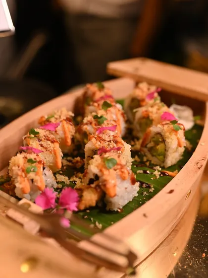 A beautiful wooden boat filled with our Asparagus & Tempura Sushi, topped with crispy bits and edible flowers, ready to be served at our live sushi bar.