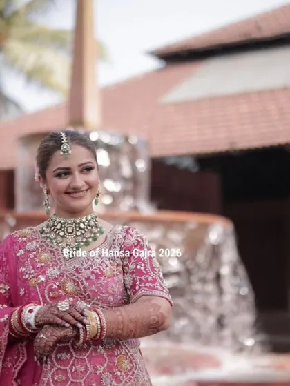 A radiant bride smiling in front of a fountain. Her hands, adorned with mehendi and jewelry, are gracefully held together, completing her stunning bridal portrait.
