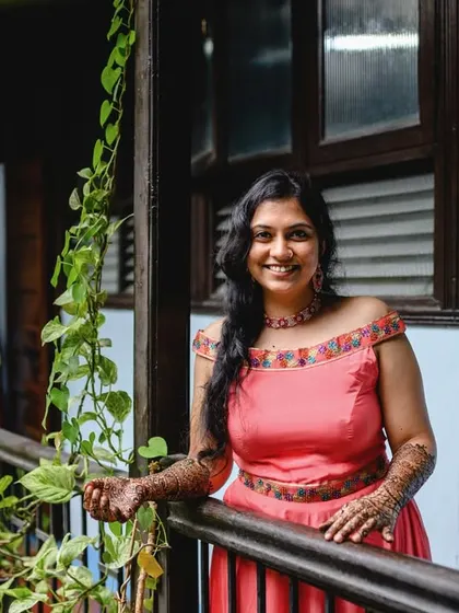 A portrait of Poorva on the balcony of her family's wada. The traditional architecture and greenery provide a beautiful backdrop.
