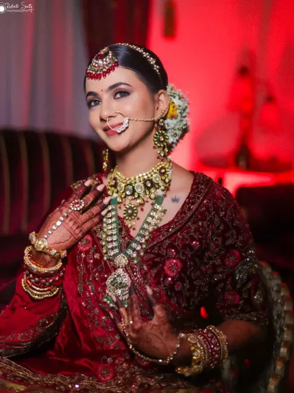 A happy and radiant bridal portrait. The bride's smile, combined with her elaborate jewelry and the warm red lighting, creates a joyful and celebratory image.