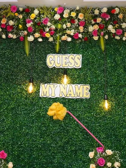 A lush green wall serves as the backdrop for this naming ceremony. It's framed with a thick border of fresh roses and baby's breath, with hanging bulbs for a warm glow.