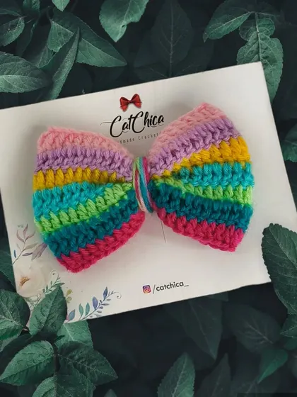 Our rainbow hair bow, beautifully photographed against a background of green leaves.