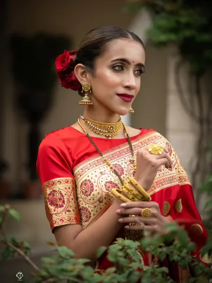 An artistic portrait with the model framed by green leaves, creating a beautiful contrast with her red saree.
